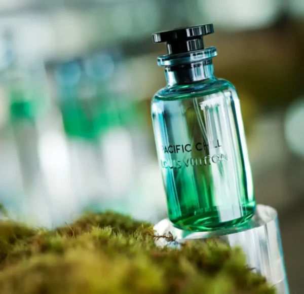 Butelka perfum Louis Vuitton Pacific Chill w odcieniach zieleni i błękitu, umieszczona na przezroczystej podstawce pośród zielonego mchu.