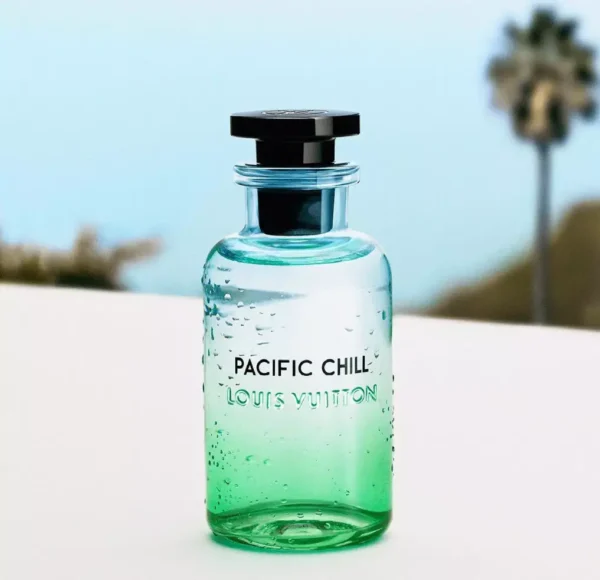 Flakon perfum Louis Vuitton Pacific Chill z kropelkami wody na zielono-niebieskim szkle, stojący na białej powierzchni. W tle rozmyta plaża z palmą.