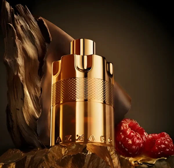 Złoty flakon perfum Azzaro Wanted Elixir, stojący na skalistej powierzchni obok dwóch malin i kawałka drewna, na ciepłym, brązowym tle.