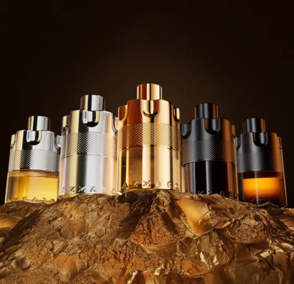 Pięć flakonów perfum Azzaro Wanted w kształcie bębenka rewolweru, w różnych kolorach (złoty, srebrny, czarny), stojących na pofałdowanym, złotym materiale.