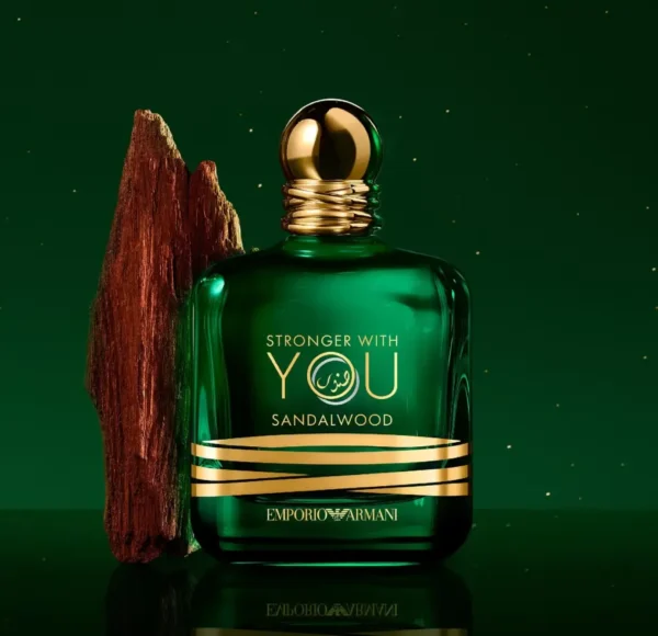 Flakon perfum Emporio Armani Stronger with You Sandalwood w kolorze ciemnozielonym, z rzeźbionym drewnem sandałowym obok, na zielonym tle.
