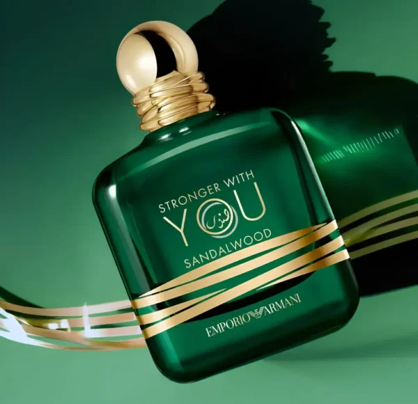 Flakon perfum Emporio Armani Stronger with You Sandalwood w kolorze ciemnozielonym, z rzeźbionym drewnem sandałowym obok, na zielonym tle.