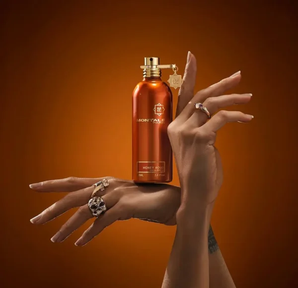 Miedziany flakon perfum Montale Honey Aoud, z zawieszką w kształcie gwiazdy, trzymany w dwóch dłoniach z pierścionkami na palcach.