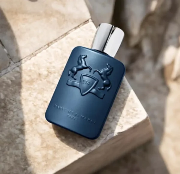 Matowy, granatowy flakon perfum Parfums de Marly Layton, leżący na jasnym, kamiennym bloku w naturalnym, ciepłym świetle. Ujęcie z góry podkreśla luksusowy charakter zapachu i jego wytłaczane logo.
